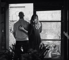 a man and woman standing in front of a window looking out at the yard outside