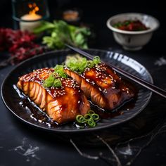 two pieces of salmon on a black plate with chopsticks and garnishes