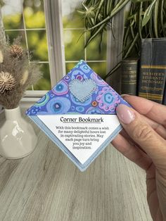 a person holding up a card in front of a window with books on the table