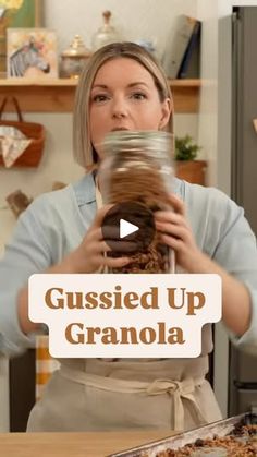 a woman in an apron holding a jar filled with granola