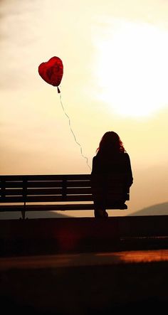 a person sitting on a bench with a heart shaped balloon