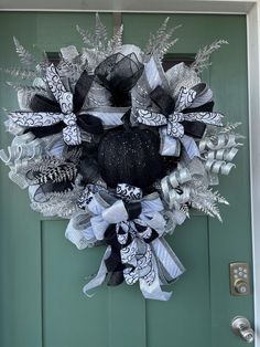 a black and white wreath hanging on a green door with silver ribbon around the wreath