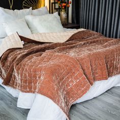 a bed covered in blankets and pillows on top of a wooden floor next to a night stand