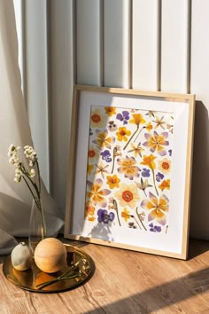 a vase with flowers sitting on a table next to a framed painting and two eggs