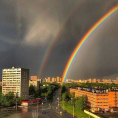 two rainbows are in the sky over a city with tall buildings and green trees