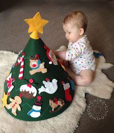 a baby is sitting on the floor next to a christmas tree shaped like a cone