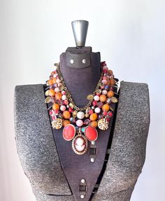 How stunning is this bright jewel tone piece? As we head into fall, I am still focused on incorporating as much color as possible into my style of work.  You can never go wrong with orange or cameos during the fall!  I have had these bright vintage orange beads for over 10 years and I finally found use for them in this stunning ensemble!  At the bottom is a repurposed vintage cameo in immaculate condition with bright red orange and dark yellow vintage earrings.  The strands are composed of big c Vintage Multicolor Jeweled Necklaces, Deco Boho, Art Deco Boho, Orange Necklace, Necklace Big, Repurposed Vintage, Vintage Cameo, Necklace Red, Gold Art Deco