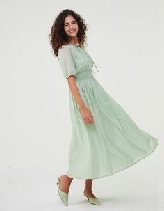 a woman in a green dress is smiling at the camera with her hand on her hip