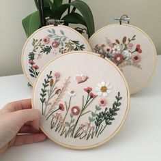 two embroidered hoops with flowers and leaves on them are being held by a person