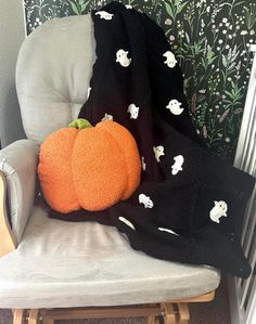 an orange pumpkin sitting on top of a chair next to a black and white blanket