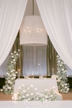 a table with flowers and candles under a chandelier in front of a window