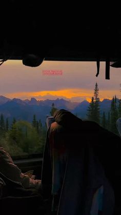 two people are sitting on a train looking out the window at mountains and trees in the distance