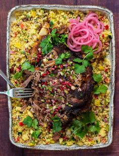 a dish with meat, rice and vegetables in it on a wooden table next to a fork