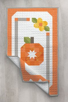 an orange and white quilted wall hanging on the side of a cement wall next to a vase with flowers