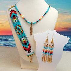 two necklaces and earrings are on display near the ocean at sunset, with an orange sky in the background