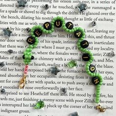 a green beaded bracelet with black letters and charms on top of an open book