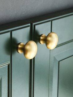 two brass knobs on green cabinets in a room with gray walls and flooring