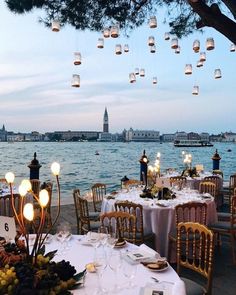 an outdoor dining area overlooking the water with lanterns hanging from it's ceiling and tables covered in white tablecloths