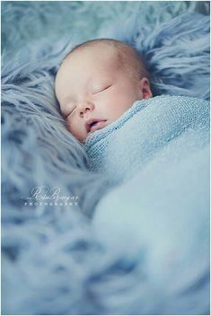 a newborn baby wrapped in a blue blanket sleeping on top of it's side