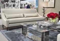 a living room filled with furniture and flowers on top of a glass table in front of a fireplace