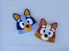 two crocheted hats with different colored animals on them, one is blue and the other is red