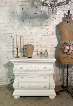 a white chest of drawers next to a mannequin with flowers on it and candles