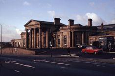 a red car parked in front of a large building on the side of a road