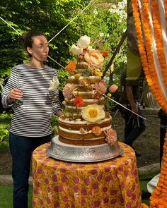 a woman standing in front of a tall cake on top of a table covered in flowers