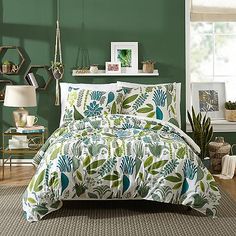 a bed with green and white comforter in a room next to a potted plant