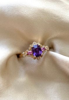 an engagement ring with purple stones in it on a white satin background, close up