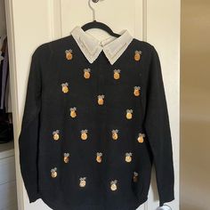 a black sweater with pineapples on it is hanging from a hanger in front of a door