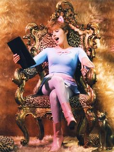 a woman sitting in a leopard print chair holding a book and looking at the camera