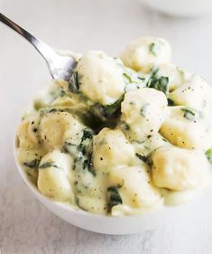 a white bowl filled with dumplings and spinach on top of a marble table