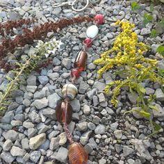 several beads and stones on the ground next to some plants with yellow flowers in the background