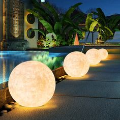 three large white balls sitting on top of a sidewalk next to a pool at night