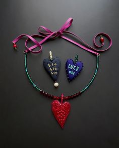 two heart shaped pendants are hanging from a string on a black surface with a pink ribbon