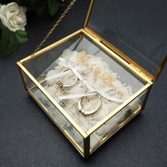 a glass box filled with wedding rings and white flowers on top of a black table