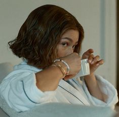 a woman sitting on a couch drinking from a cup in her hand and looking off to the side