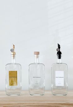 three empty glass bottles sitting on top of a wooden table next to a white wall