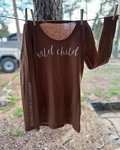 This is a brown long sleeve shirt with a white glittery vinyl lettering across the chest. The lettering on the sleeve is in silver. A unique AZ Wild Child design! Long Sleeve T-shirt With Lettering, Brown Long Sleeve Graphic T-shirt, Brown Long Sleeve Cotton T-shirt, Brown Long Sleeve Tops With Letter Print, Brown Long Sleeve Top With Letter Print, Long Sleeve Name Print Tops For Fall, Long Sleeve Tops With Name Print For Fall, Brown Long Sleeve Shirt, Prescott Az