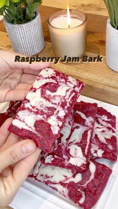 raspberry jam bark is cut into squares and placed on a plate next to a candle