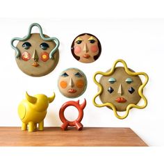 four clay faces are mounted on the wall above a wooden table with a yellow toy