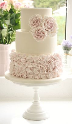 a three tiered wedding cake with pink flowers on the top and bottom, sitting in front of a window