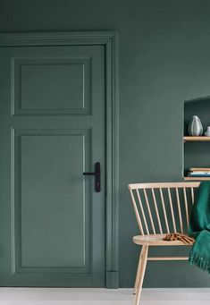 a green door in a room with a chair and bookshelf next to it