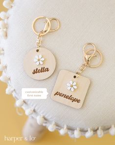 two wooden keychains with name tags attached to them on a white cushioned surface