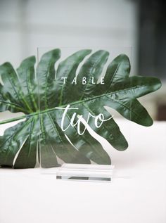 a table sign with a green leaf on it that says table two in white lettering