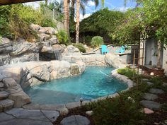 an outdoor swimming pool surrounded by rocks and palm trees