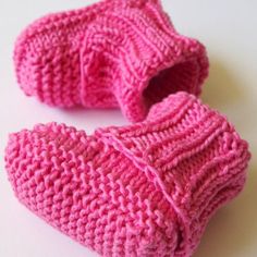 two pink knitted mittens sitting on top of a white table next to each other