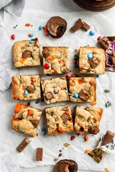 chocolate chip cookie bars cut into squares on top of white paper with candy and candies scattered around them