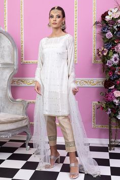 White and gold are preferred choices of Mughal princess. You can never go wrong with a classy white silhouette. Sylvia by Maria Nasir is a classic wardrobe piece for a reason! This elegant piece defines femininity and can make you look beautiful effortlessly. Sylvia is beautiful combination of pearl white and gold A-line shirt in paper cotton fabric. The boat neckline is dazzled with gold lace while the ¾ sleeves are also adorned with gold lace. Featuring the soft organza tulle dupatta in shades of pearl white and gold. The shirt is paired with a matching silk slip and beige pants with lace detailing. Accessorize this number with ethnic earring and bindya set for a flawless look. Top: Color: White Fabric: Paper cotton A shaped shirt with zari work all over Boat shaped neckline    Gold lace Semi-stitched Gold Chanderi Lawn Suit, Elegant Churidar With Resham Embroidery For Wedding, Elegant Wedding Churidar With Resham Embroidery, Gold Chanderi Dress With Dabka Detailing, Festive Wedding Organza Churidar, Elegant Chinon Churidar With Traditional Drape, Gold Anarkali Raw Silk Lawn Suit, Elegant Churidar With Chinon And Traditional Drape, Gold Anarkali Lawn Suit In Raw Silk